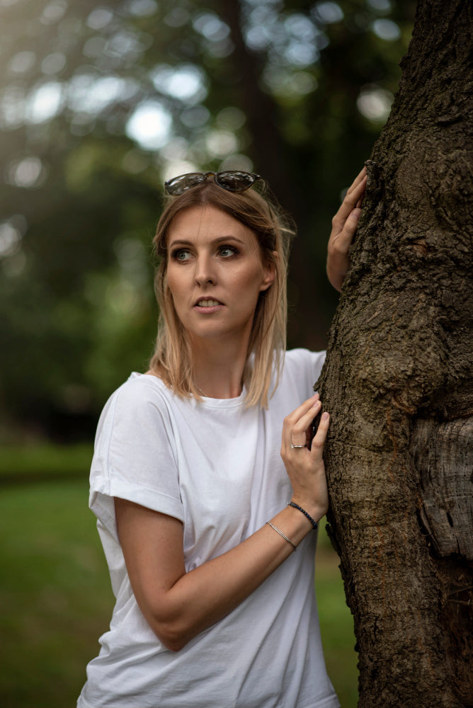 Woman in a white t-shirt standing next to a tree in a natural setting