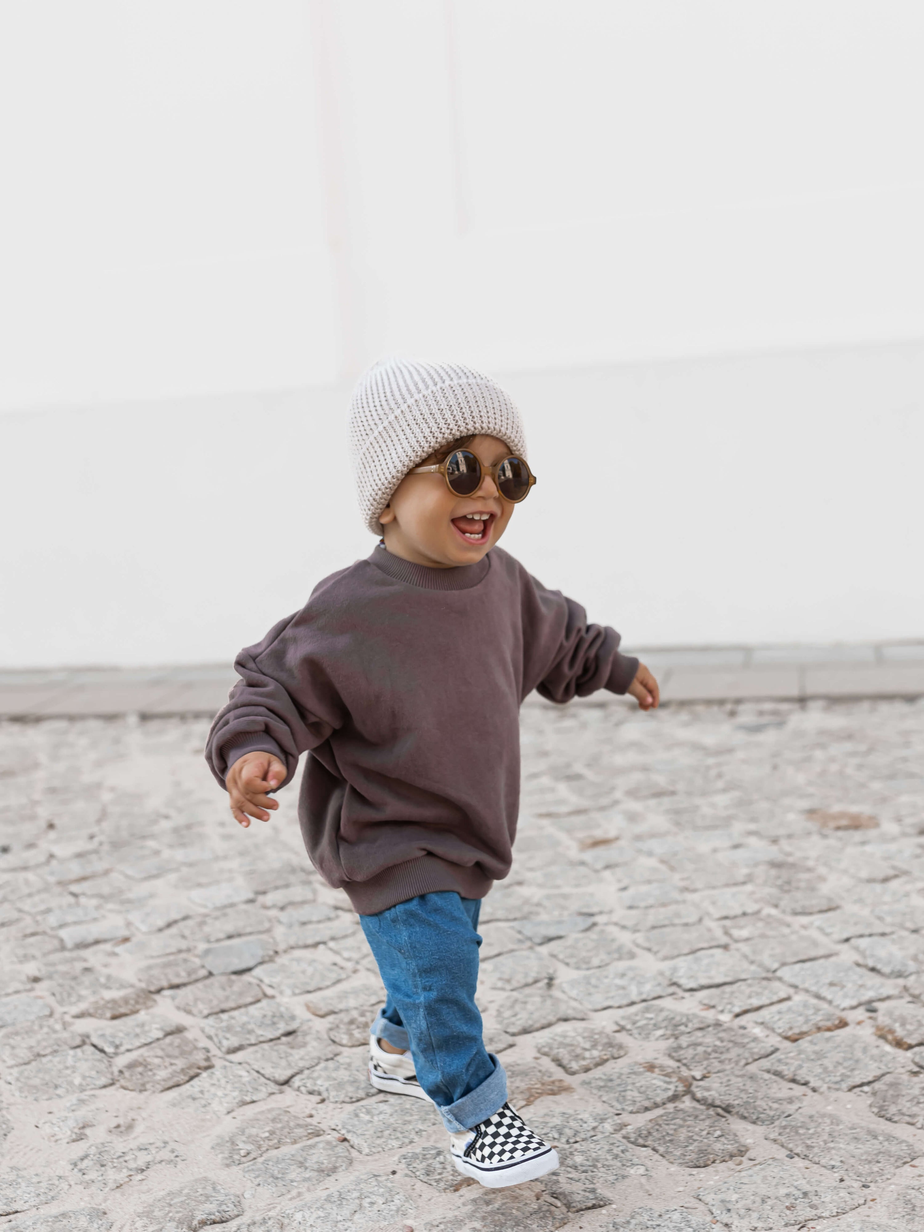 Toddler in oversized brown sweatshirt, jeans and knit beanie