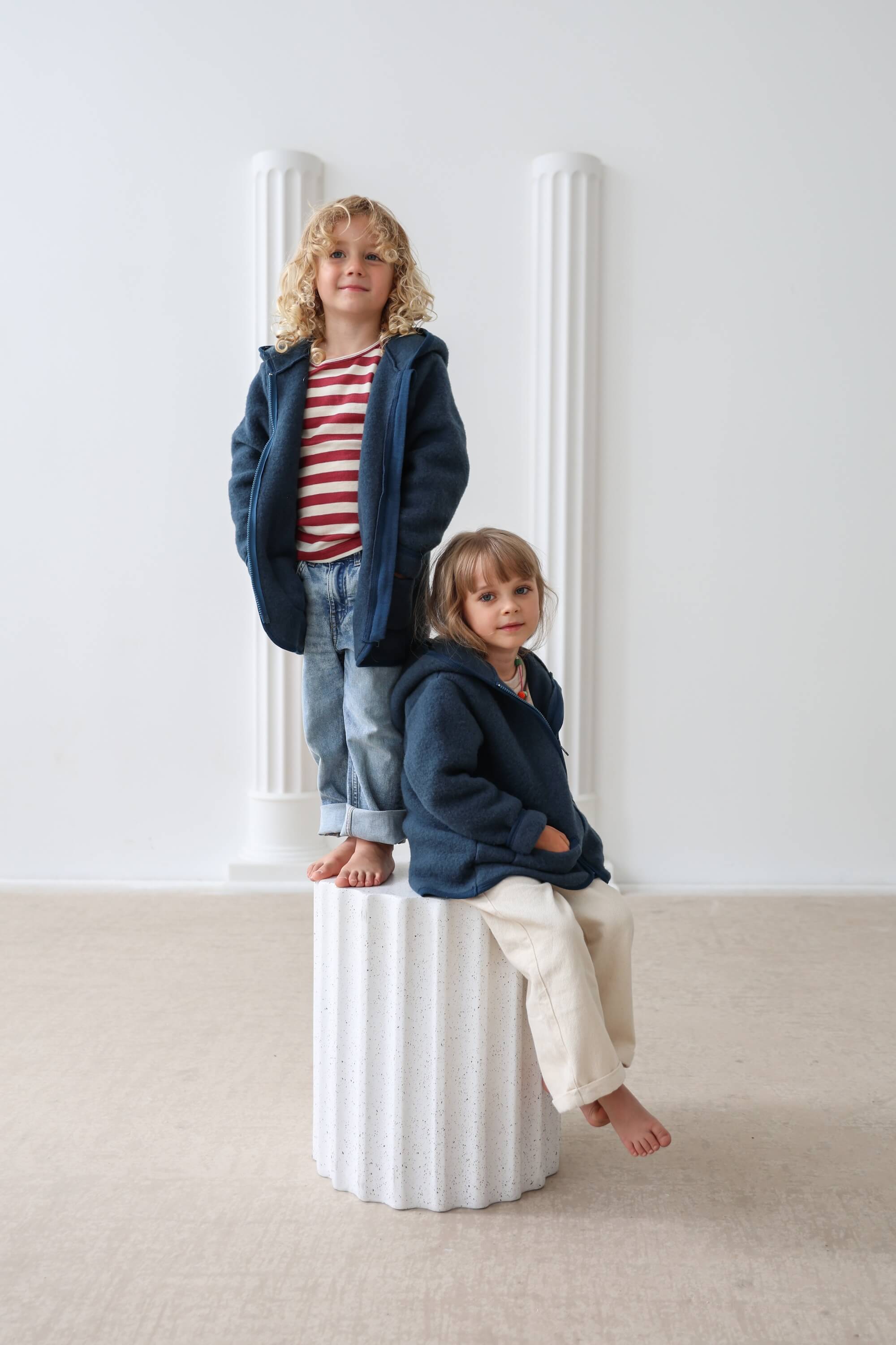 Two children wearing matching navy blue hoodies in a minimalistic setting