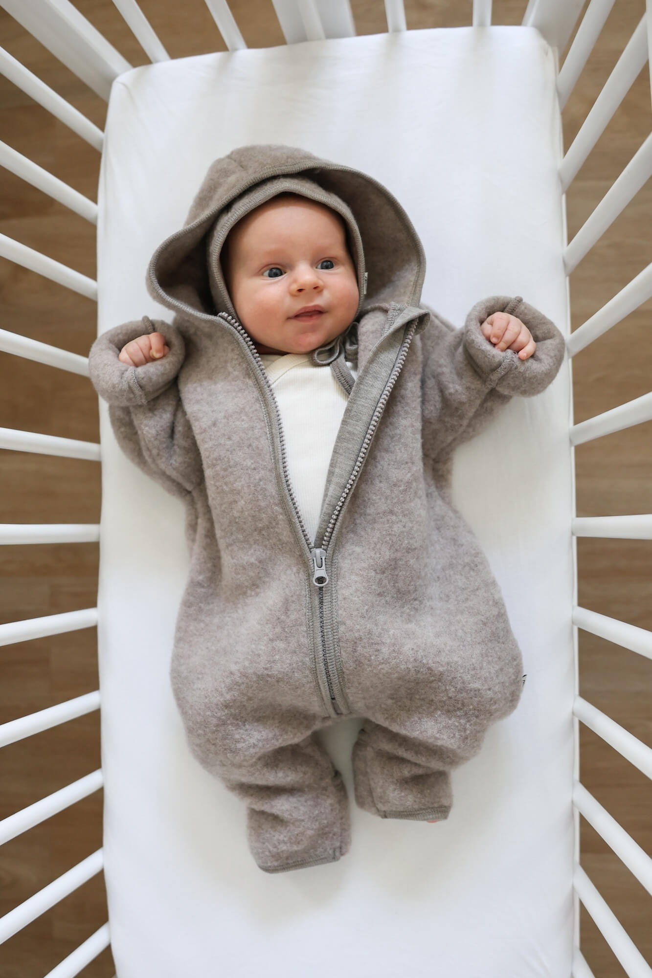 Baby in a gray onesie with a hood lying in a crib