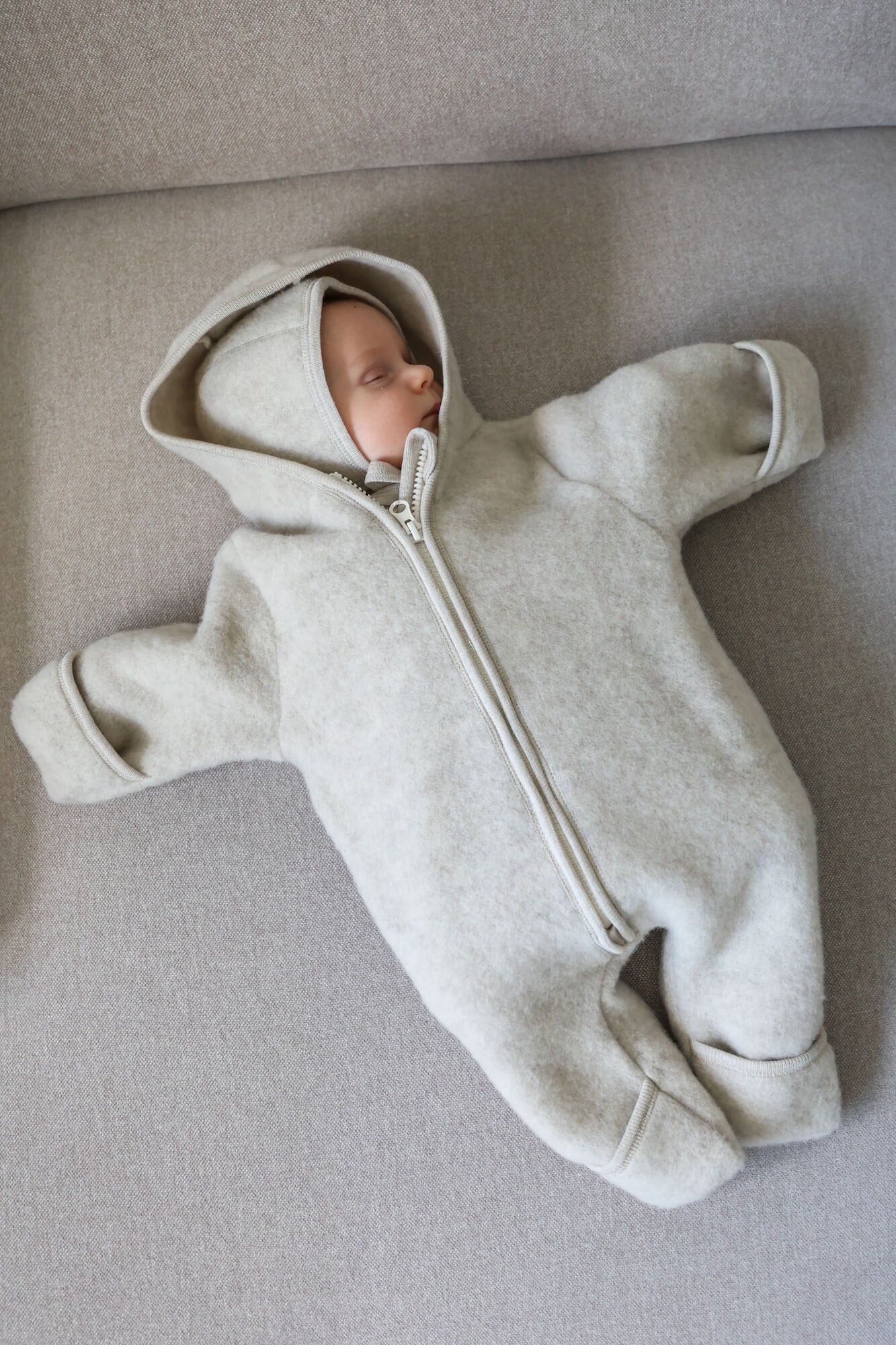 Baby in a gray onesie lying on a gray surface