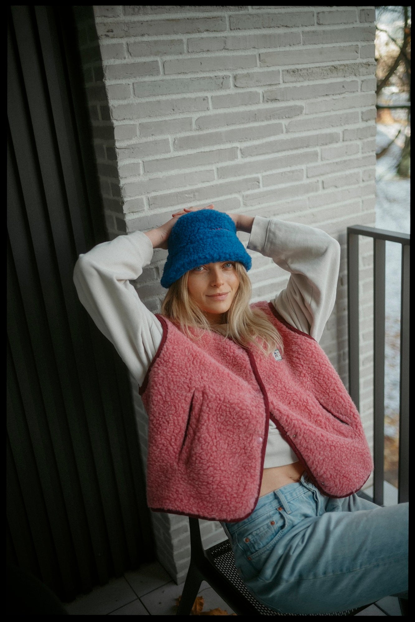 Woman in pink fleece vest and blue bucket hat on balcony