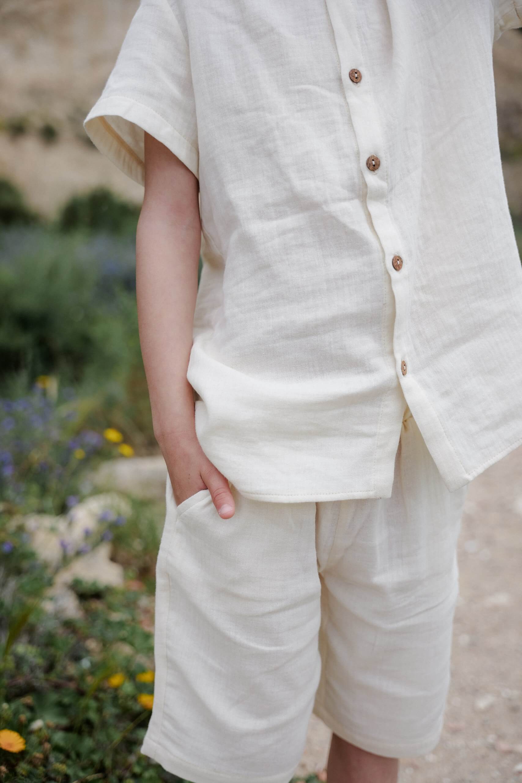 Child wearing beige cotton shorts and a matching top is standing outdoors