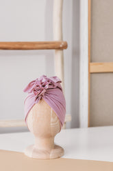 a pink turban on a wooden mannequin with wooden rack and white wall in the  background