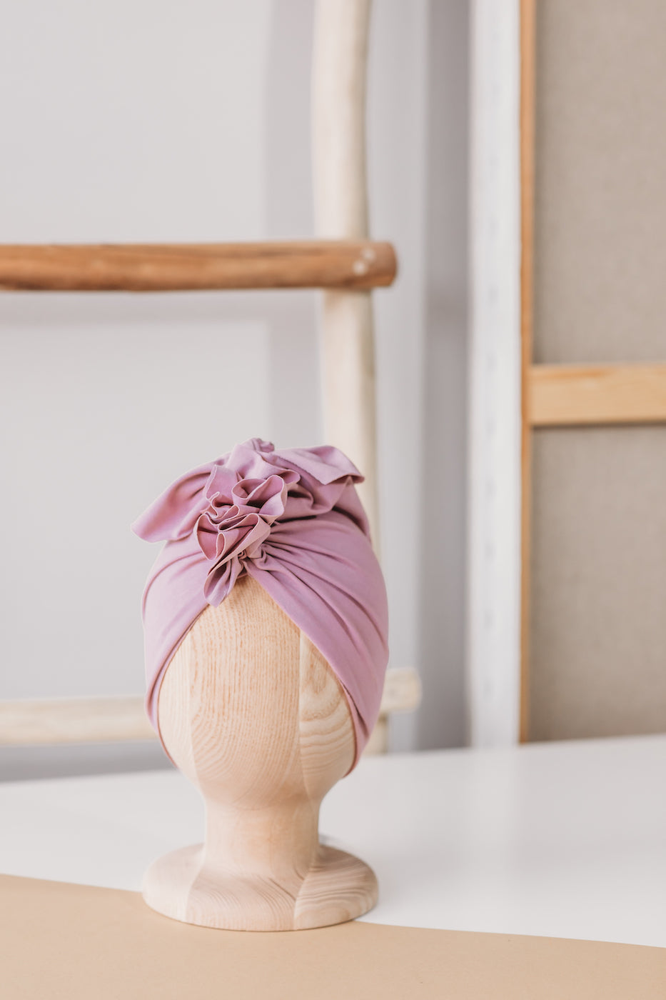 a pink turban on a wooden mannequin with wooden rack and white wall in the background
