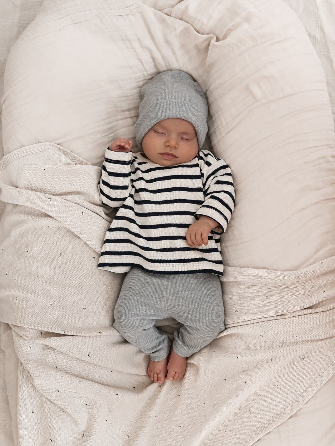 Baby lying on a bed wearing a navy striped blouse and grey leggings