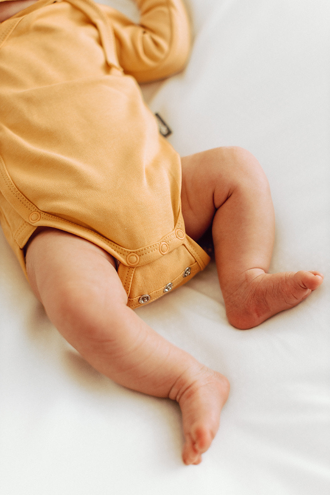 baby‘s legs and organic cotton yellow bodysuit
