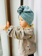 A girl wearing a velvet dusty mint turban and blouse with colorful polka dots looking out of the window