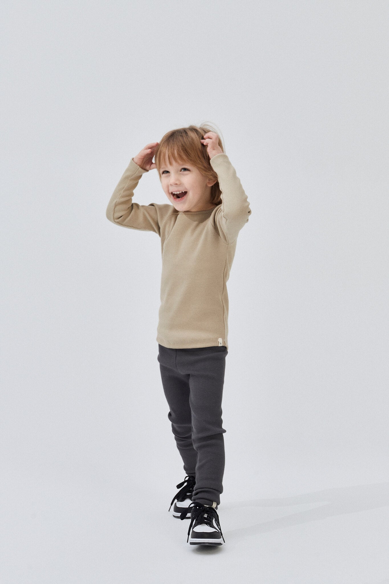 Child wearing a beige long-sleeve shirt and gray pants