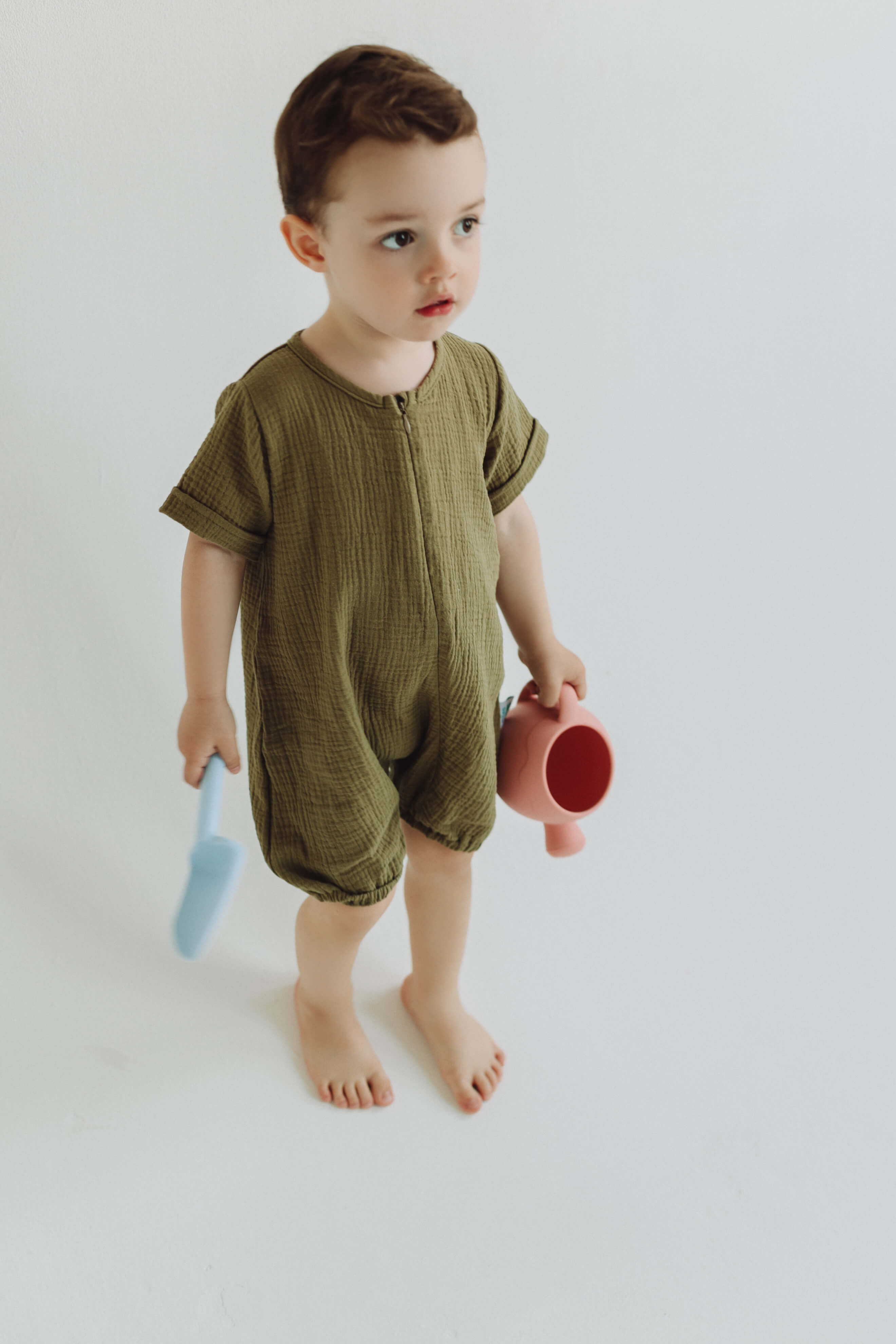 Child wearing a green romper holding a pink and red toy on a white background