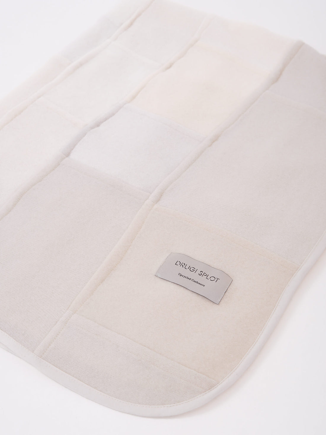 A patchwork blanket with rectangles in shades of white, ecru and beige laid out on a white background.