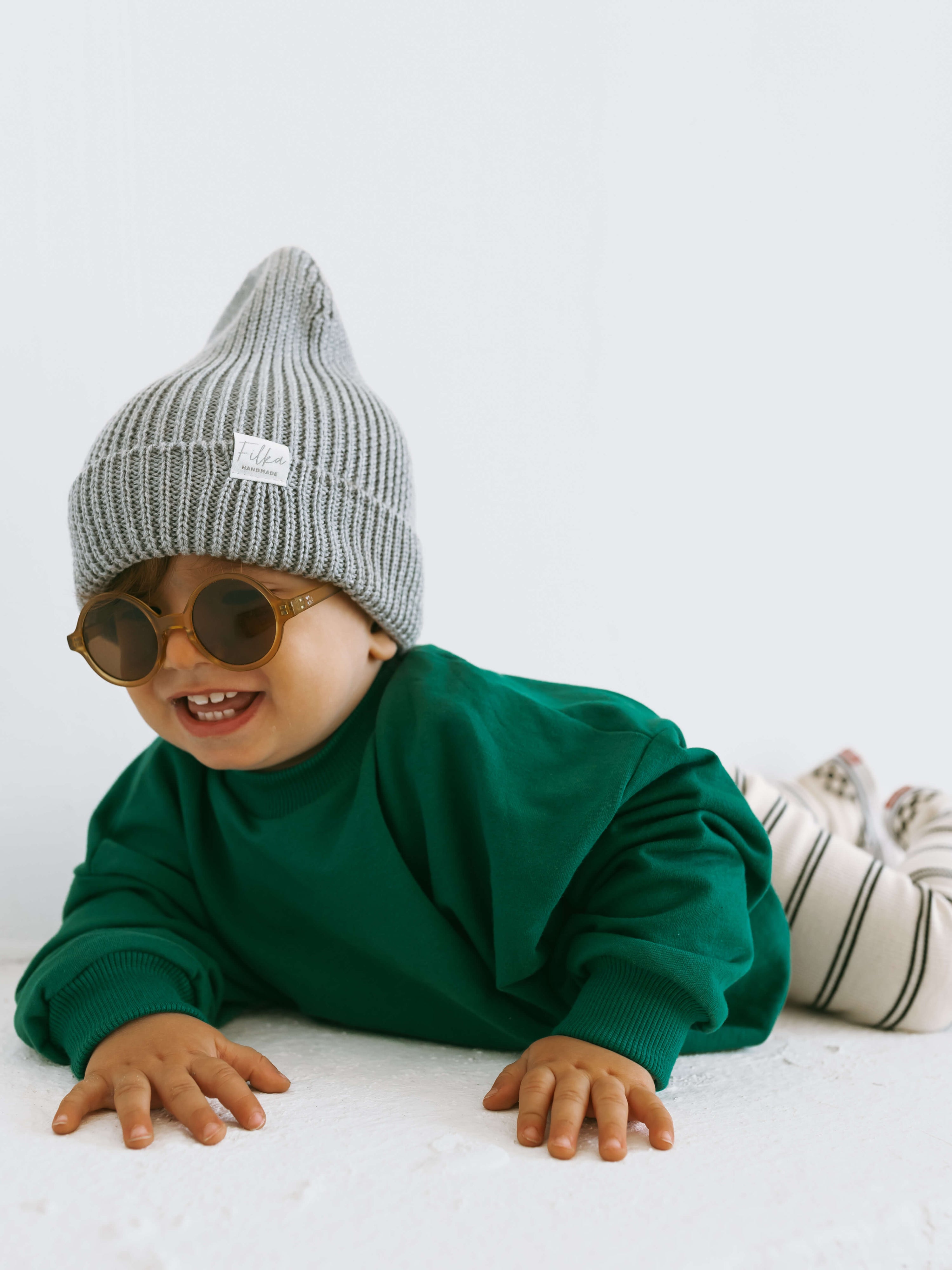 Baby wearing a green oversized sweatshirt and minimal leggings, lying on the floor