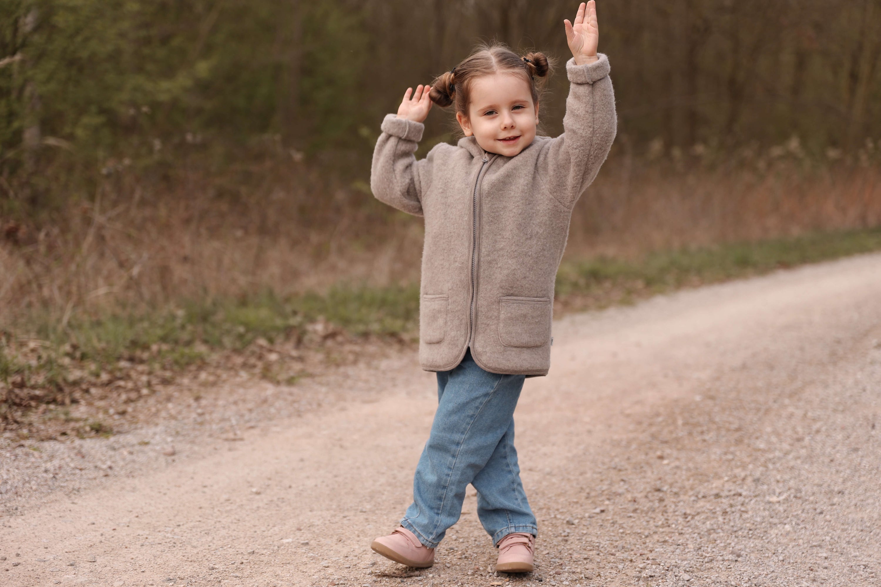 Child in a gray coat and blue jeans standing on a dirt path
