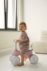 Child playing with a pink balance bike in a bright room wearing pink set