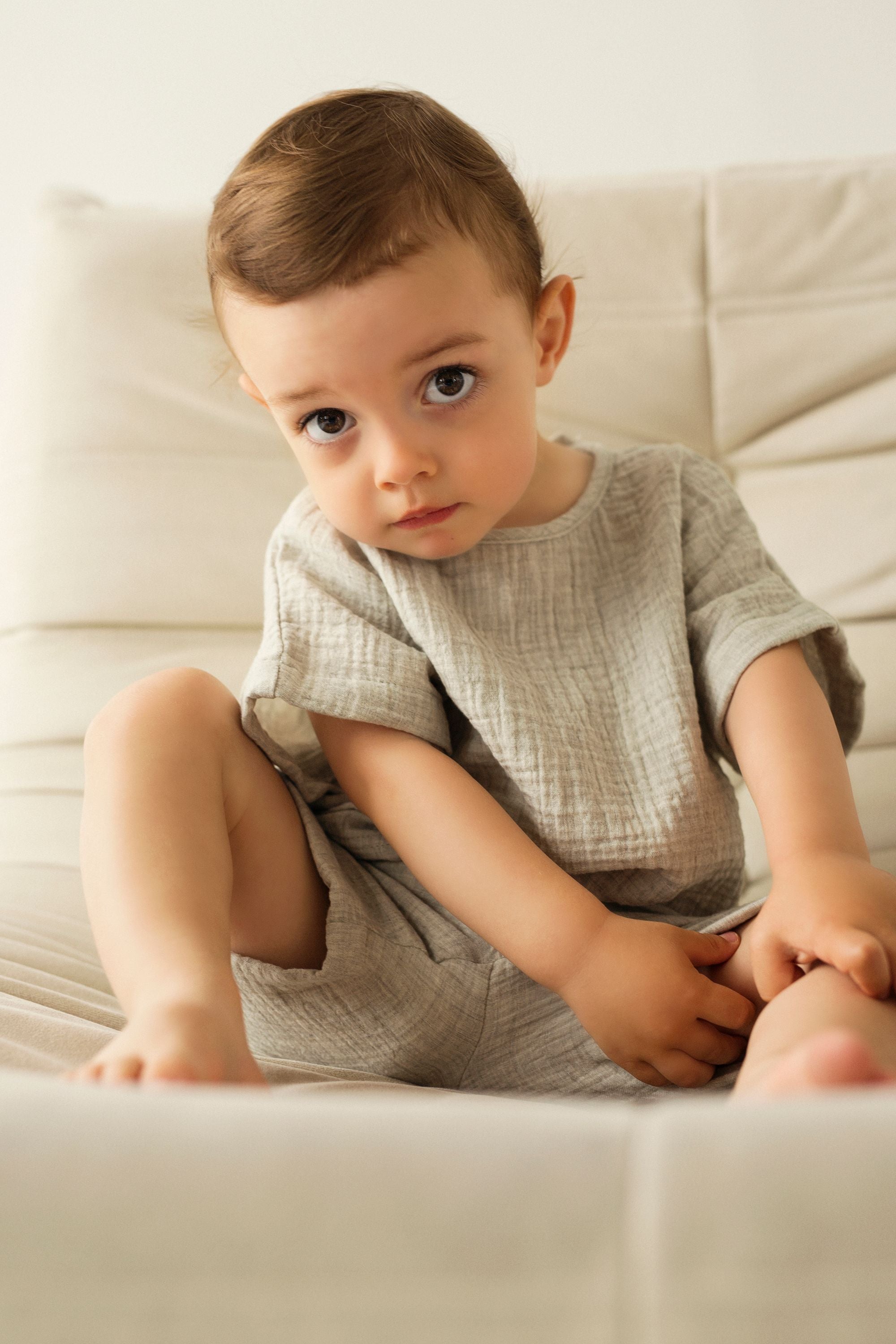 Young child sitting on a light-colored couch wearing a textured shirt and shorts