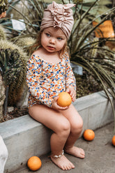 Ein sitzende Mädchen angezogen in bunten Swimmanzug  und beige Mütze Turbane hält ein Orange.