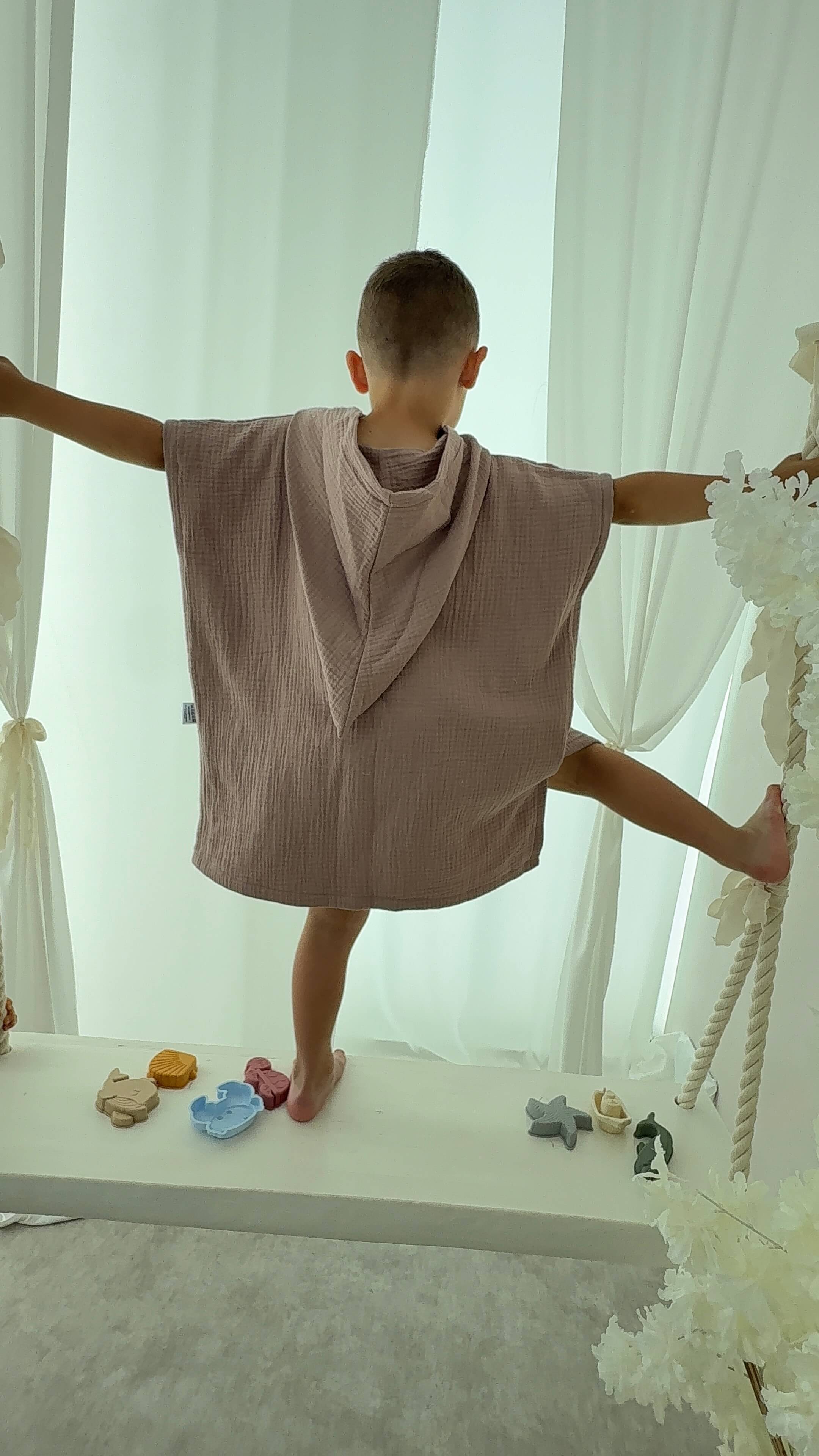 Boy wearing a beige towel over their shoulders with a white curtain background