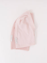 Two folded light pink beanies with small white tags on a plain white background.