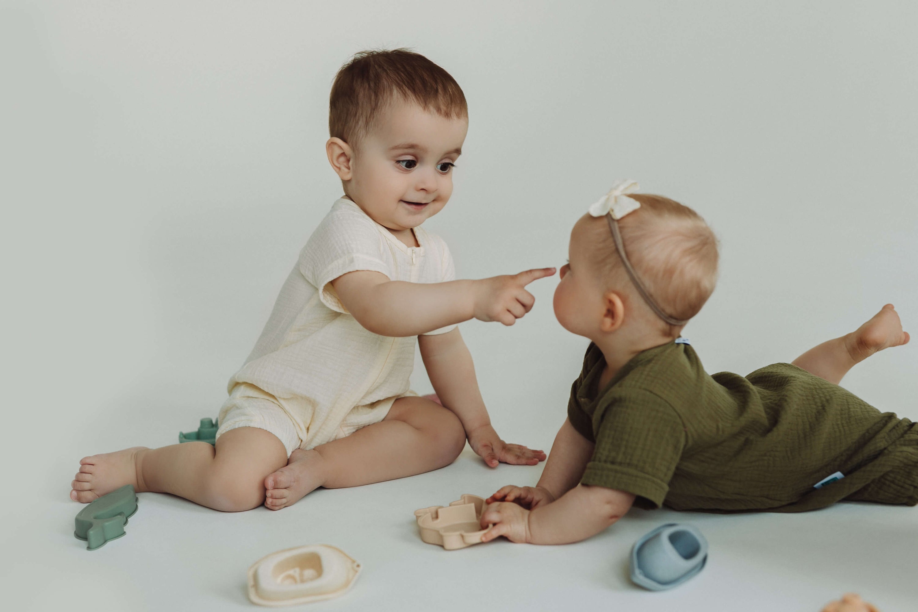 Two babies playing with toys on a plain background