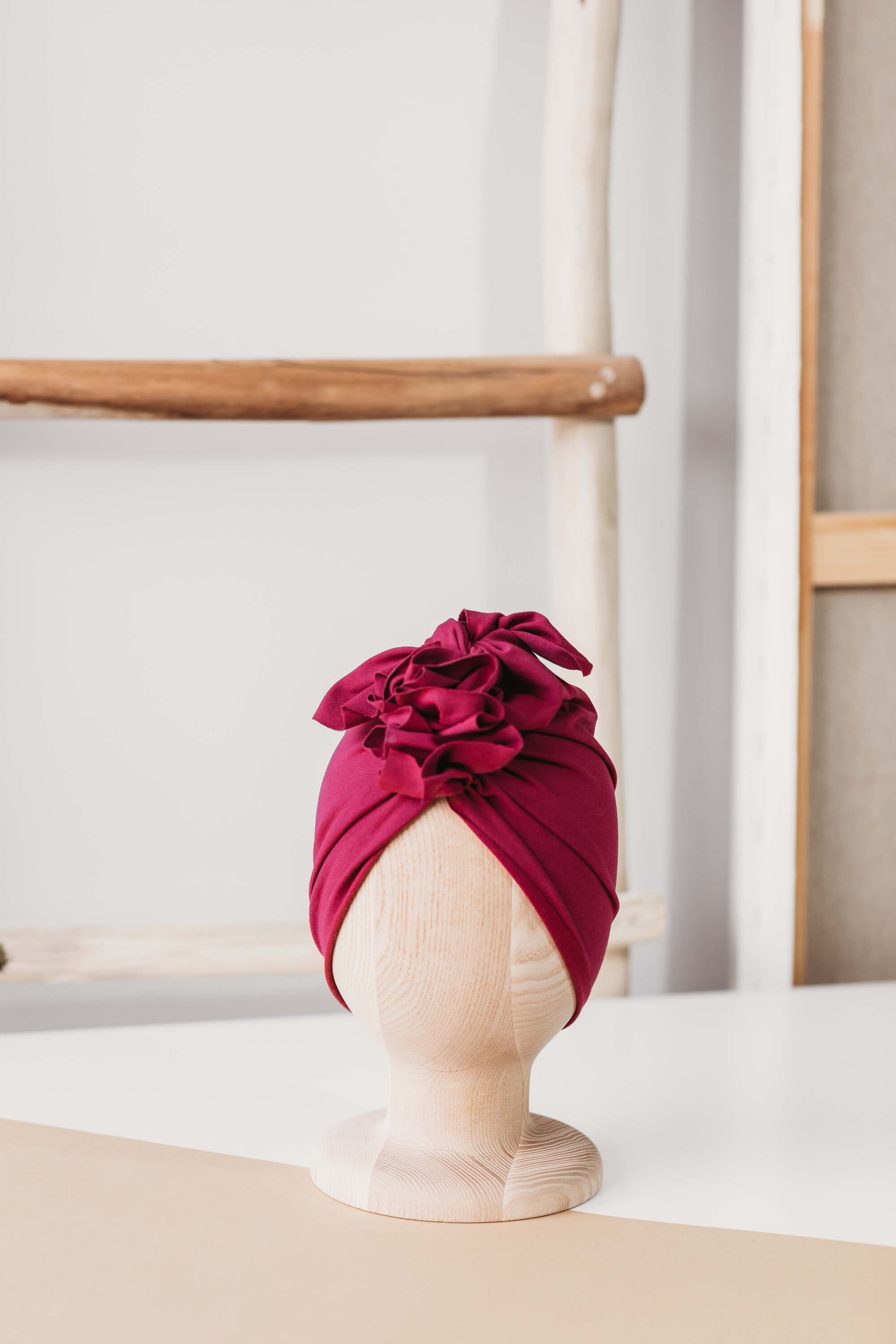 A dark red turban for children on a wooden mannequin on a white background