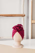 A dark red  turban for children on a wooden mannequin on a white background