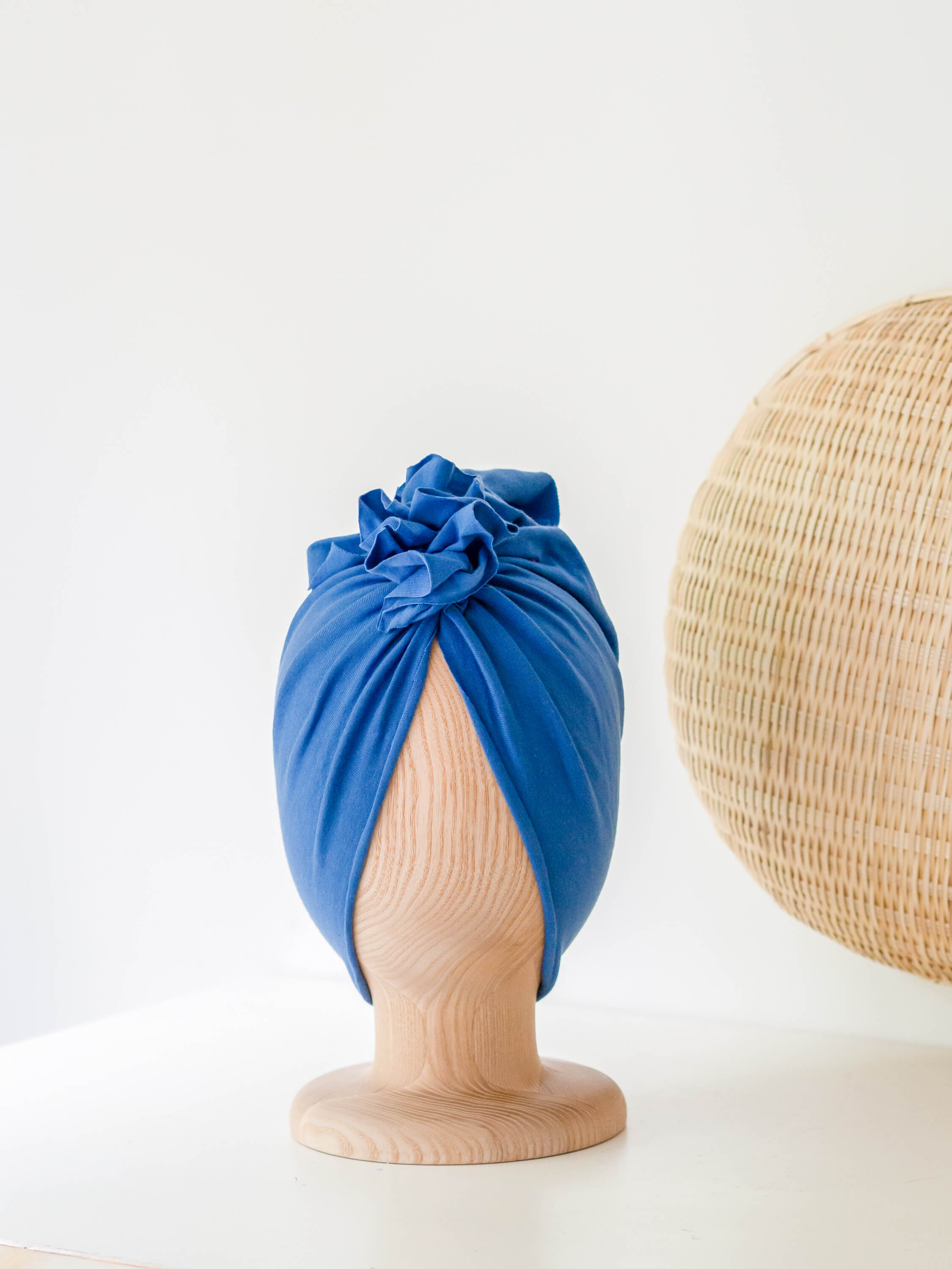 A steel blue turban for children on a wooden mannequin on a white background with a rattan decoration
