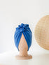 A steel blue turban for children on a wooden mannequin on a white background with a rattan decoration