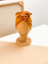 A mustrad turban for kids on a wooden mannequin standing on a beige white counter