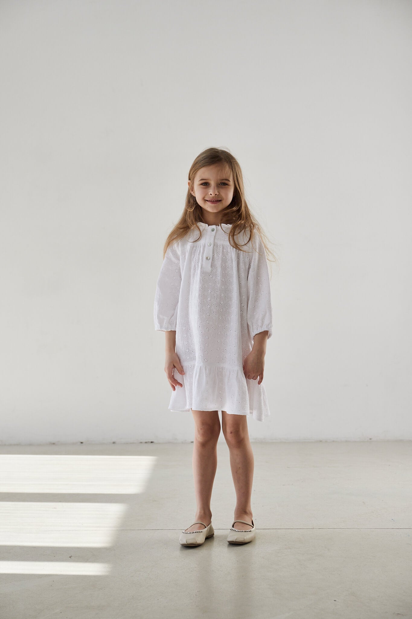 Young child wearing a vintage off white, long sleeve, knee length dress with a bow detail at the neckline