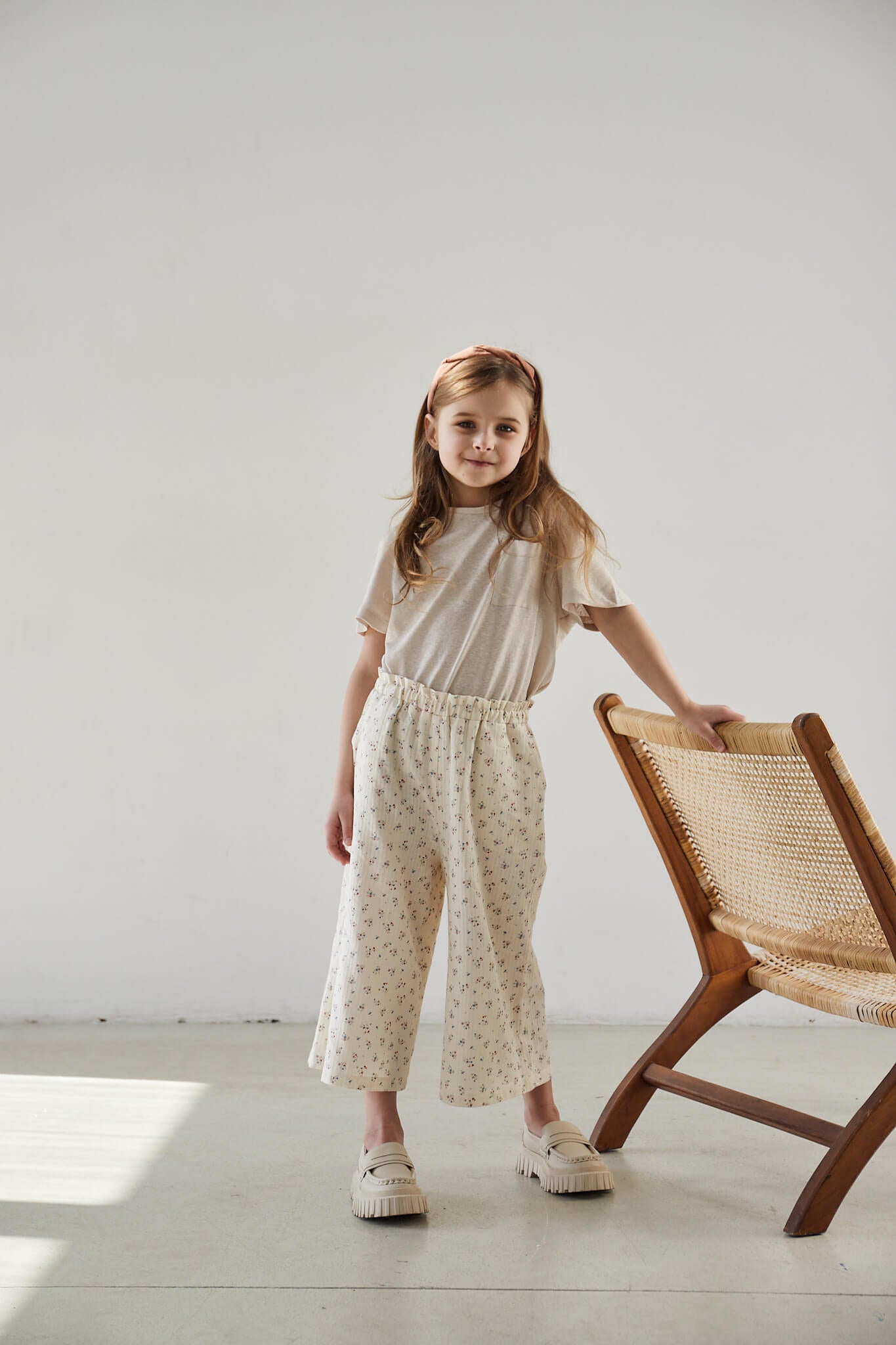 Child standing next to a chair, wearing wide-leg floral print pants and a matching top