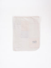A patchwork blanket with rectangles in shades of white, ecru and beige laid out on a white background.