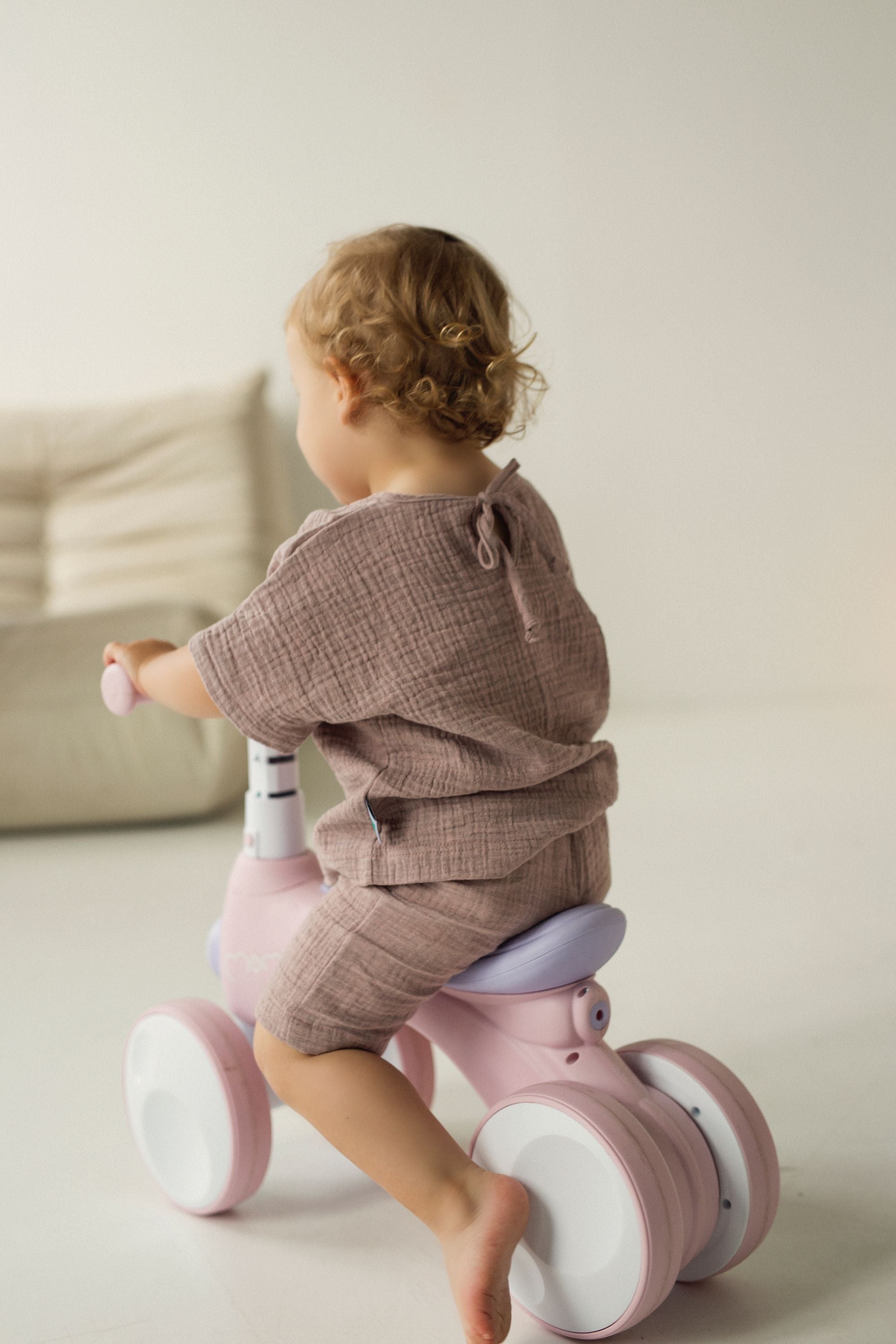 Child sitting on a pink balance bike indoors