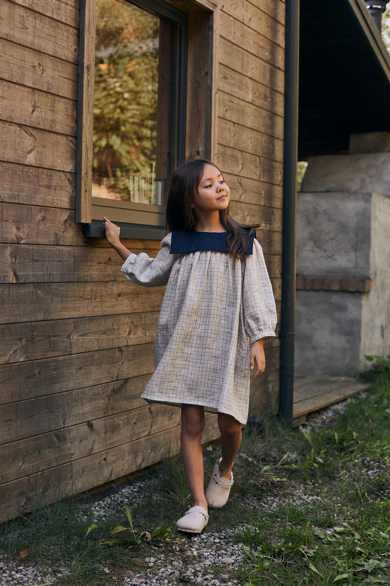 Child wearing a navy blue oversized linen dress with long sleeves and white sneakers