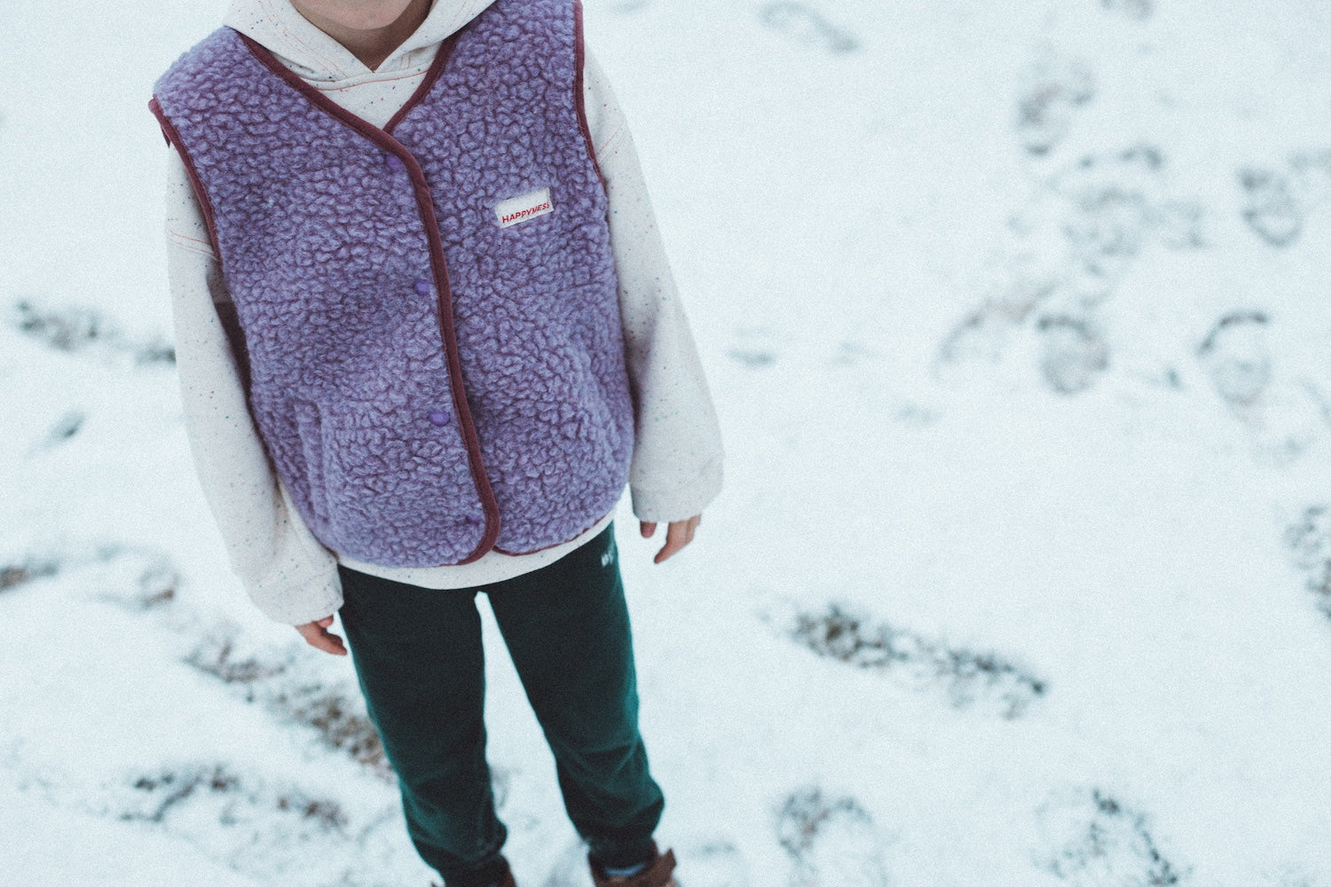 boy wearing merino wool vest and white sweatshirt standing on the snow
