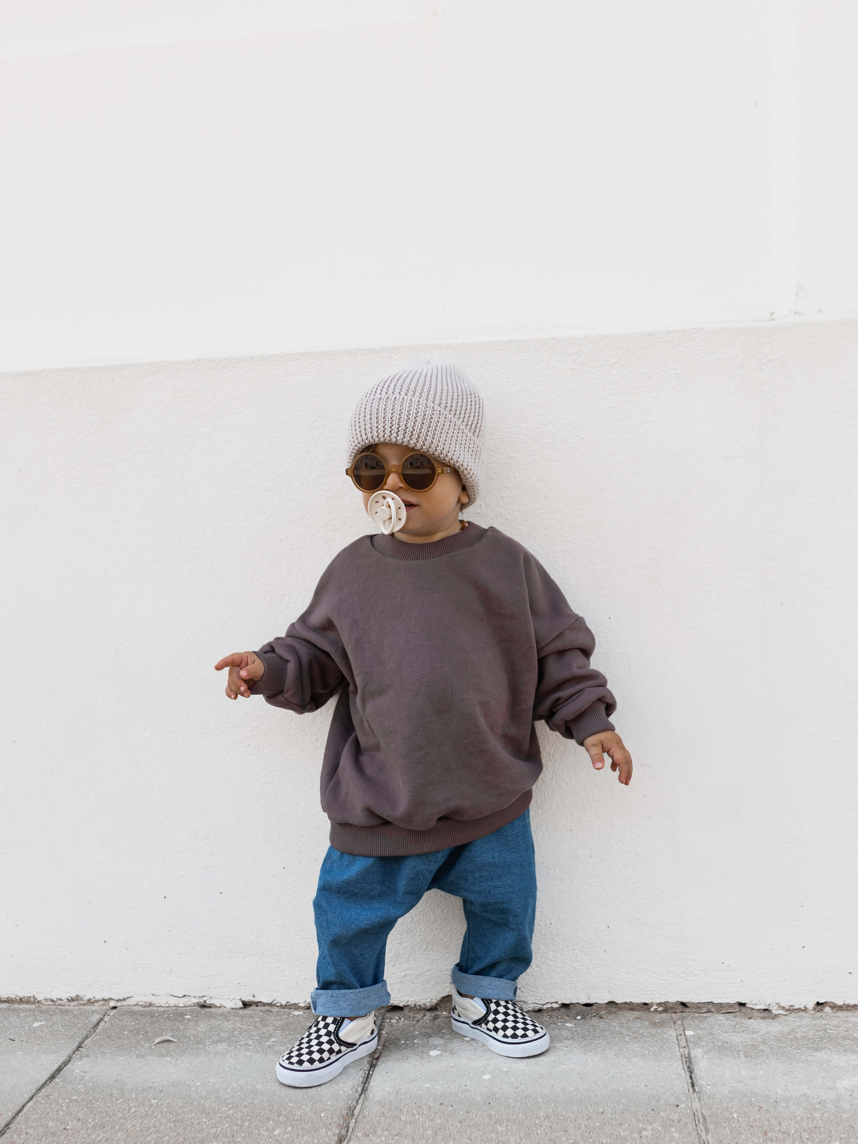 Child wearing blue jeans pants with rolled-up cuffs, a gray sweater, and checkered shoes