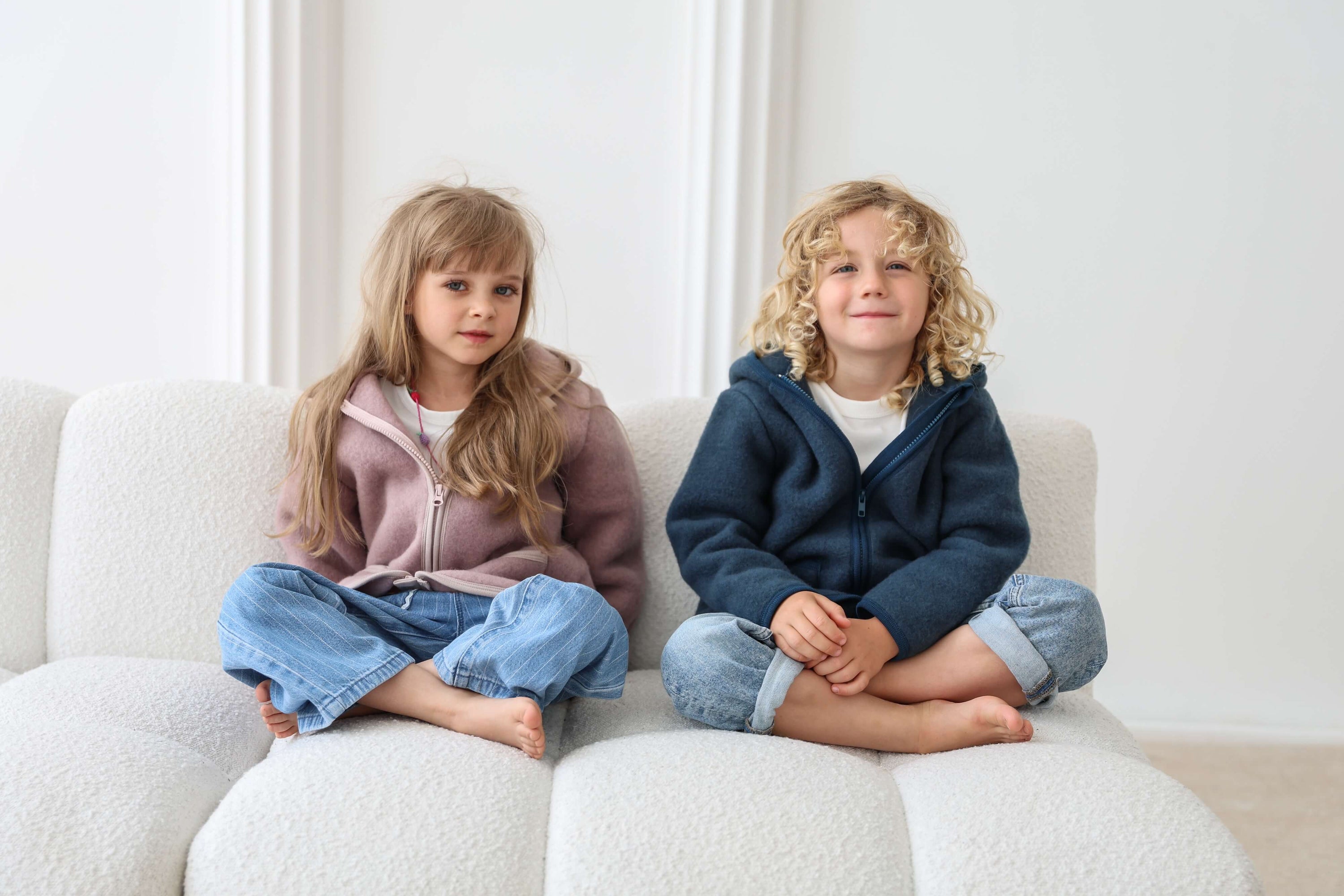 Two children sitting on a white couch in a bright room.