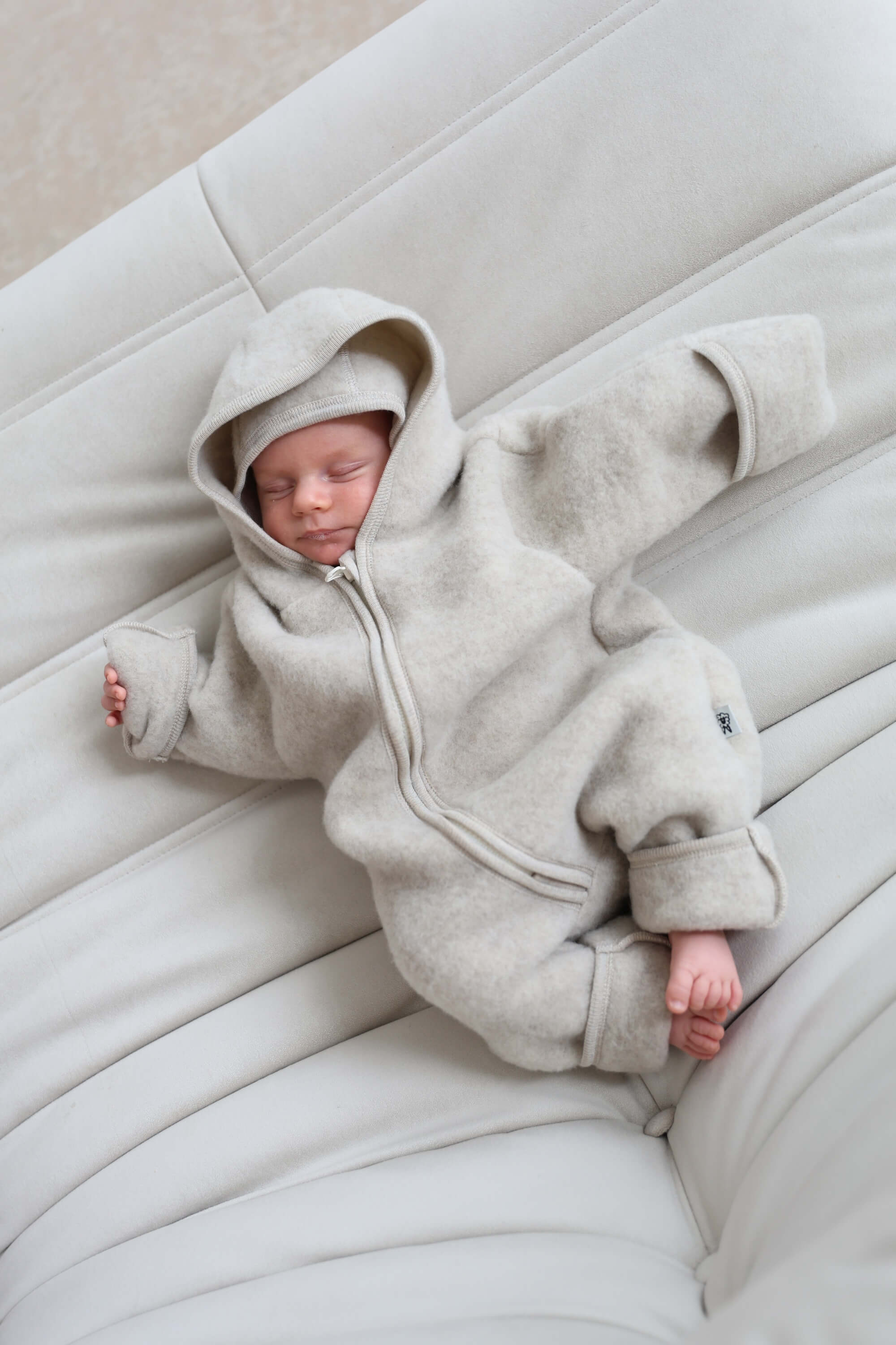 Newborn baby in a light gray hooded outfit lying on a white cushion