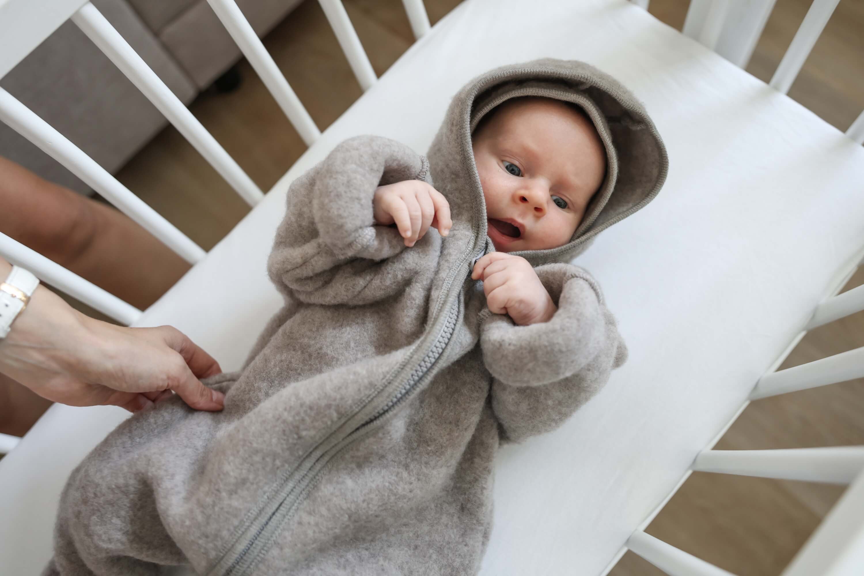 Baby in a gray hooded onesie lying in a crib