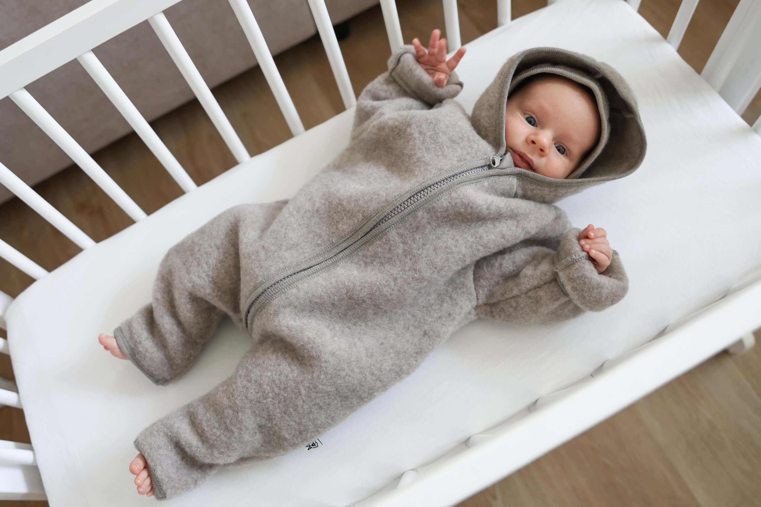 Baby in a gray onesie lying on a white crib