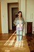 Young girl standing in a sunlit room wearing a patterned outfit.