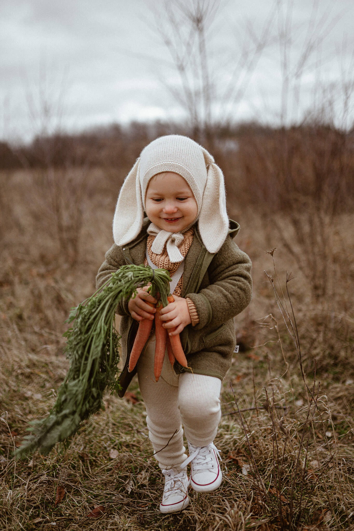Child in a field wearing a bunny outfit holding carrots