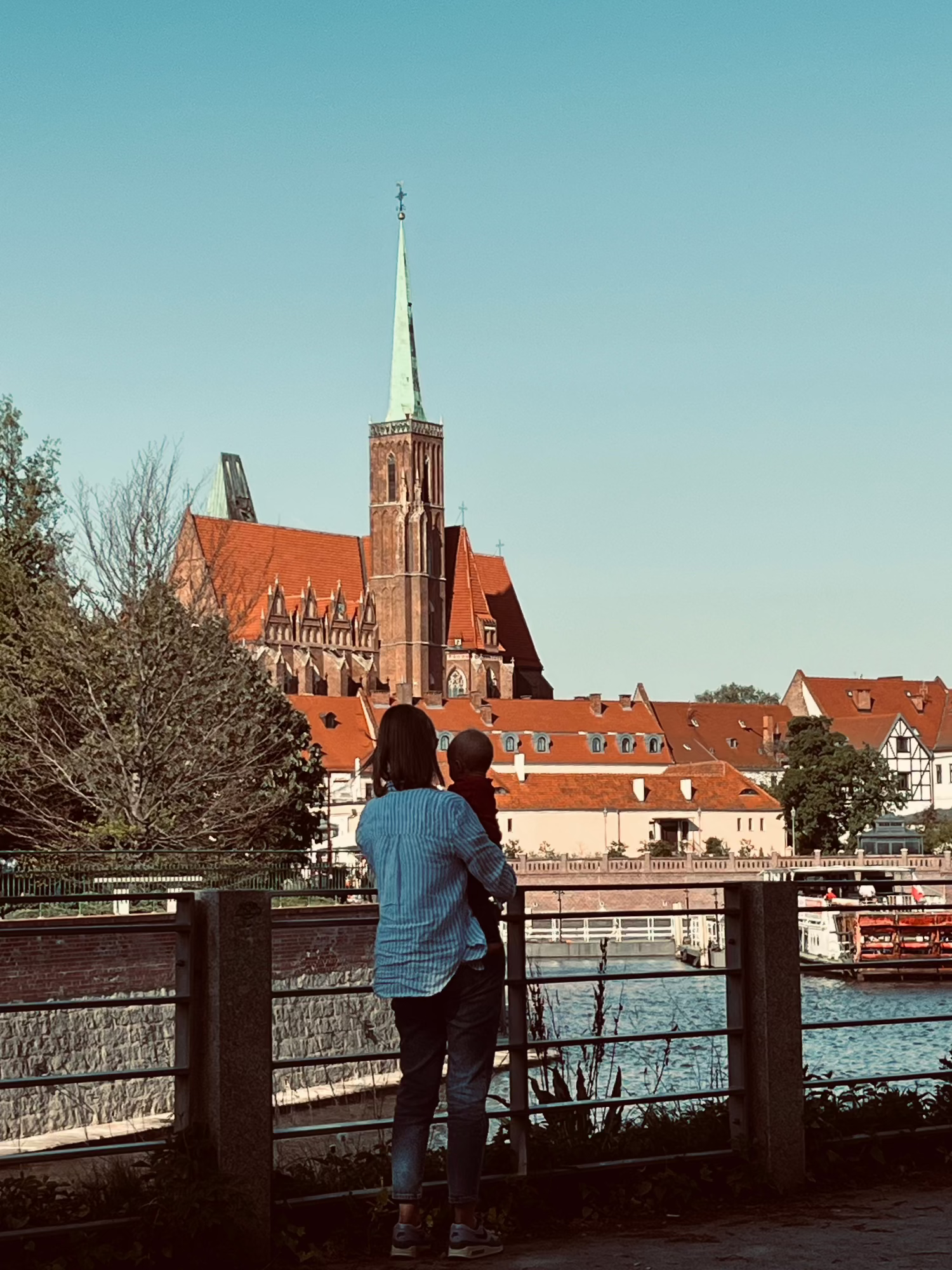 Mother holding child by riverside, looking at old church