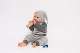 Baby in a gray onesie with bunny ears holding a wooden toy on a white background