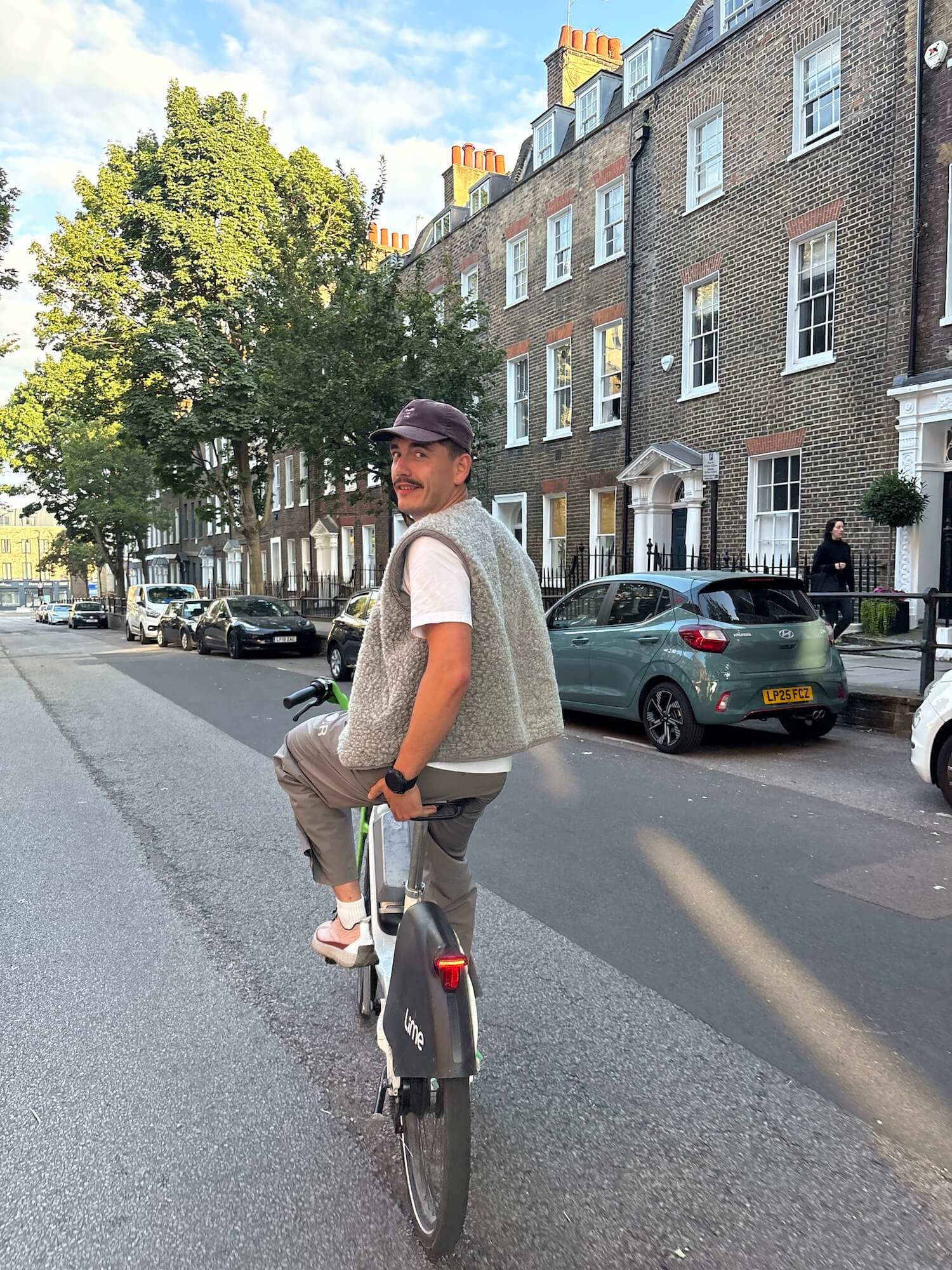 Man riding a bicycle on a street with brick buildings and trees in the background