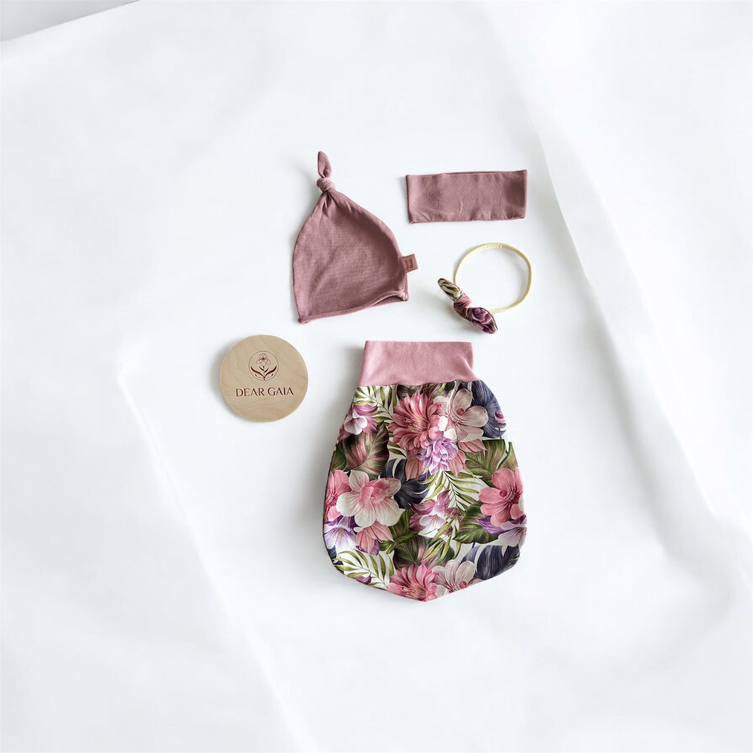 A set of preloved baby items in pink including a footbag, two headbands, and a hat with a floral pattern