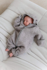 Newborn baby in a gray onesie with a hood lying on a white couch
