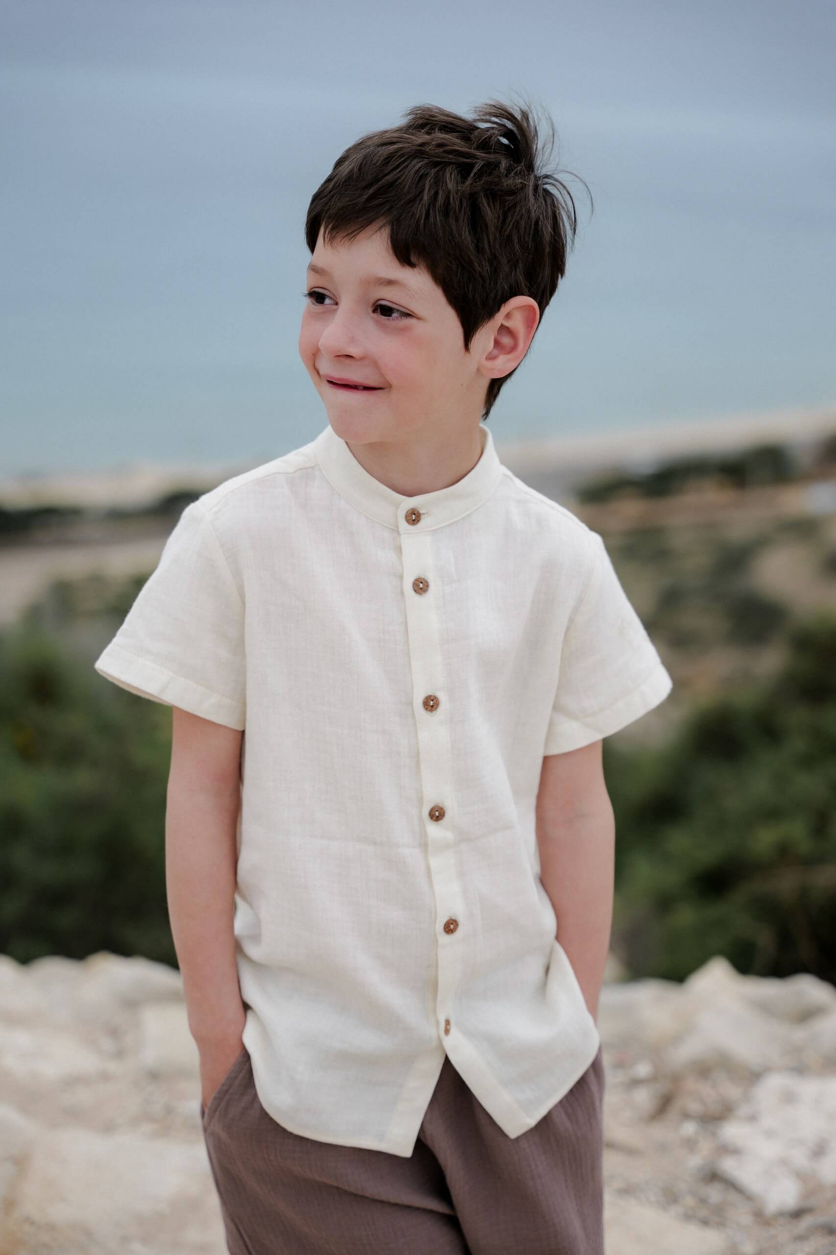 Young child wearing a short-sleeved white shirt with natural coconut buttons, standing outdoors