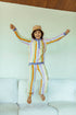 A person jumping in the air wearing striped cotton culotte pants and a matching sweatshirt, with arms raised and a happy expression.