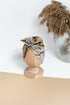 A multicolor turban for children on a wooden mannequin on a white beige background with a silver vase