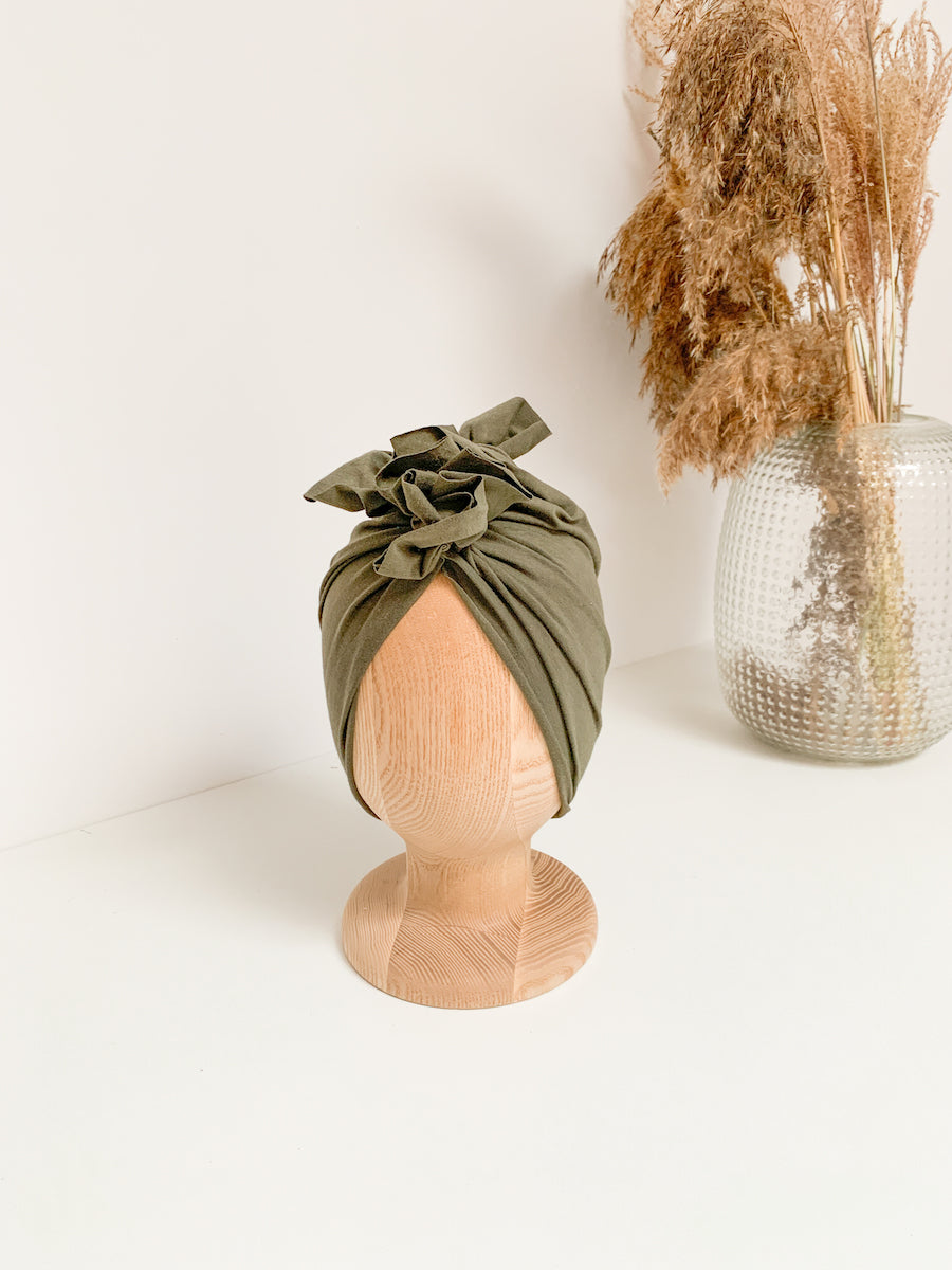 A dark green turban for children on a wooden mannequin with silver vase in the white background